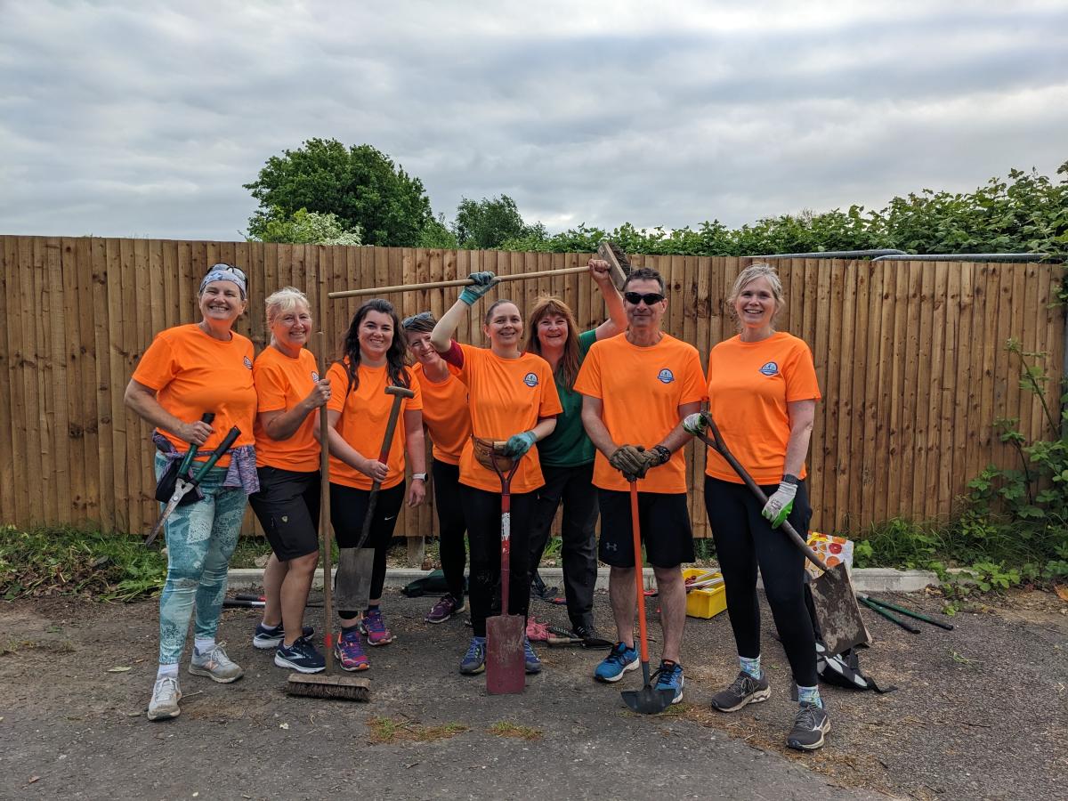 A group of 8 happy people holding gardening equipment and wearing orange T Shirts